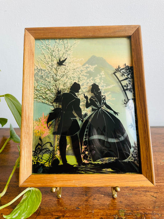 Reverse Painted Silhouette Lithograph Picture on Convex Bubble Glass - Courting Couple in Garden with Flowering Trees & Mountain View